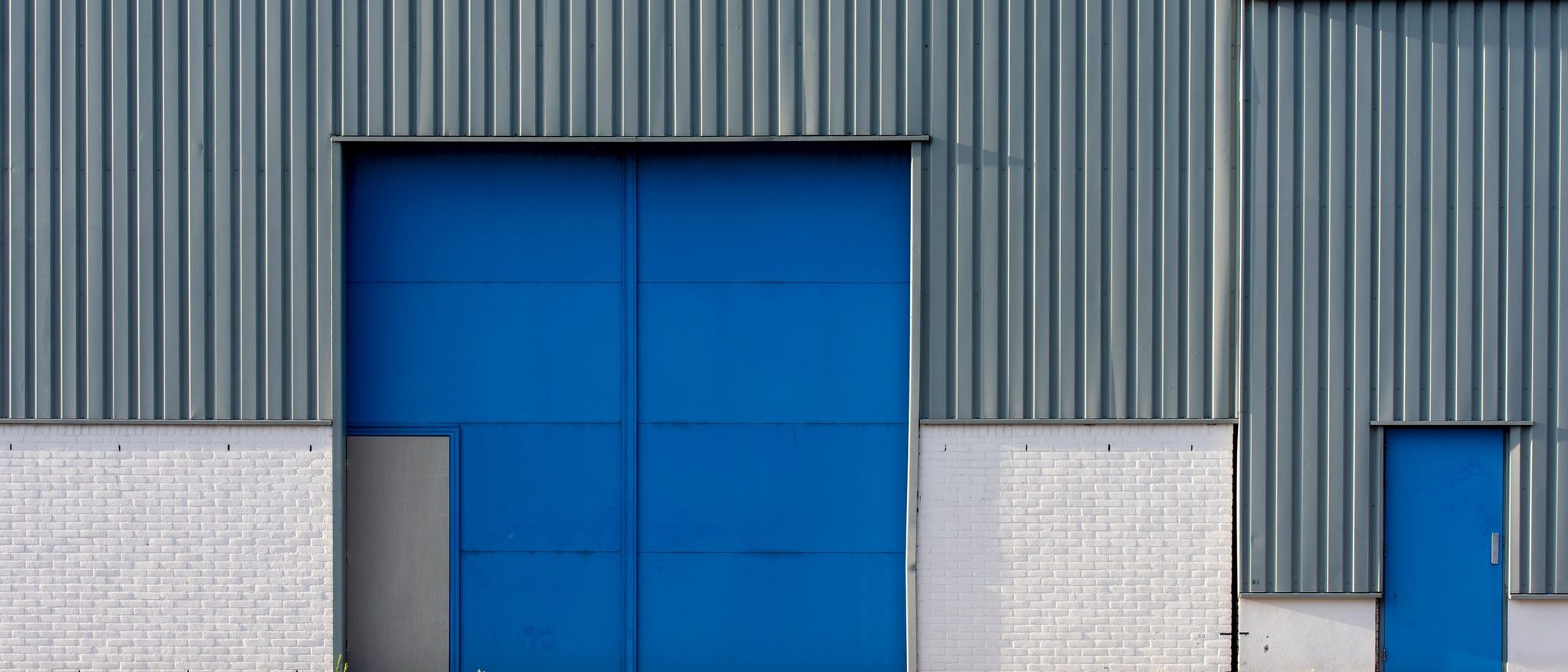 A low-rise corrugated steel warehouse with a blue roll-up door
